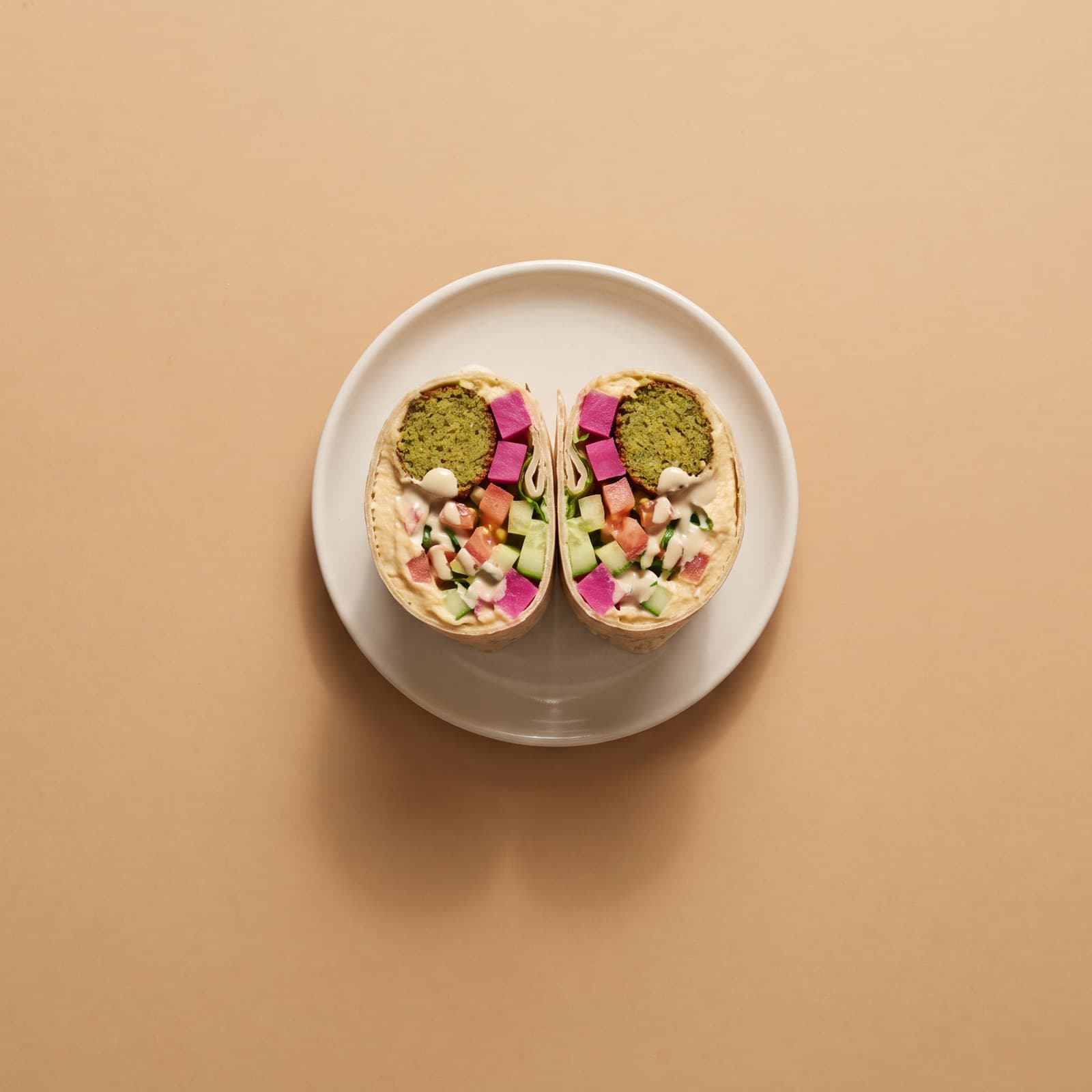 Falafelwrap halkaistuna, sisällä hummusta, pikkelöityä naurista ja tahinia